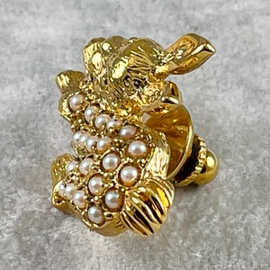 May include: A gold-toned brooch in the shape of a rabbit, adorned with white faux pearls. The rabbit is sitting up with its ears perked up and its tail curled behind it.