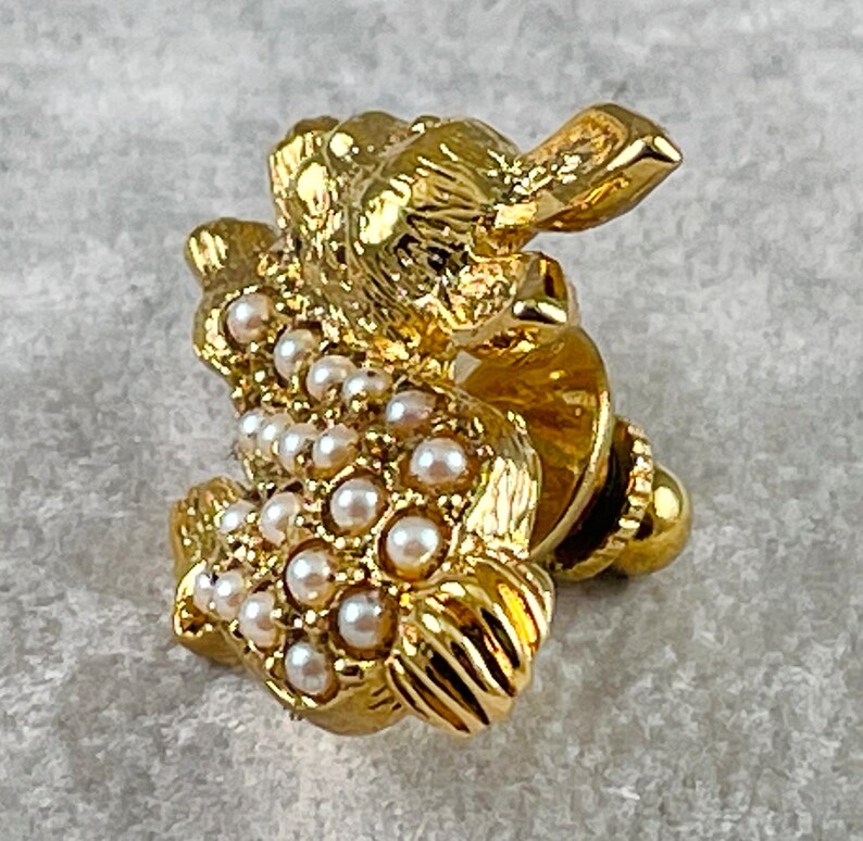 May include: A gold-toned brooch in the shape of a rabbit, adorned with white faux pearls. The rabbit is sitting up with its ears perked up and its tail curled behind it.