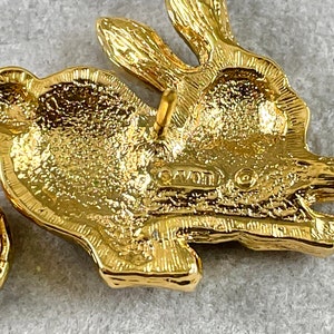 May include: Gold-toned rabbit brooch with a textured surface and a pin back. The back of the brooch is marked "Avon".
