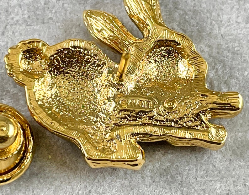May include: Gold-toned rabbit brooch with a textured surface and a pin back. The back of the brooch is marked "Avon".
