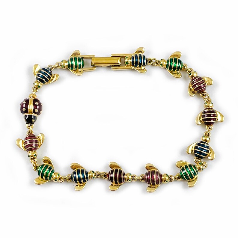 May include: A gold bracelet with a chain of small, colorful enamel ladybugs. The ladybugs are in shades of green, red, and blue.