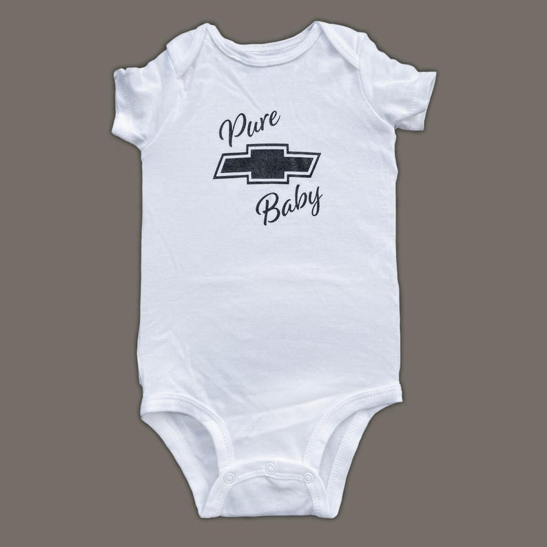 K&ouml;nnte beinhalten: Wei&szlig;er Baby-Strampler mit einem schwarzen Chevrolet-Logo und dem Text "Pure Baby" auf der Vorderseite.