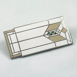 May include: A white enamel pin with a geometric design in shades of beige and green. The pin features a stylized window with a grid pattern.