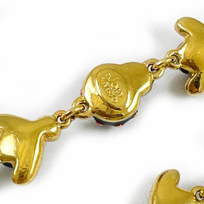 May include: Gold-tone bracelet with red and black enamel charms. The charms are shaped like a heart, a flower, and a butterfly. The bracelet has a lobster clasp closure. The charms are marked "Swarovski".
