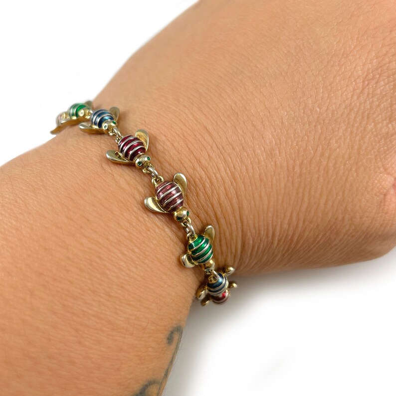 May include: A gold bracelet with a chain and colorful bee charms. The bees are red, green, and blue with gold wings.