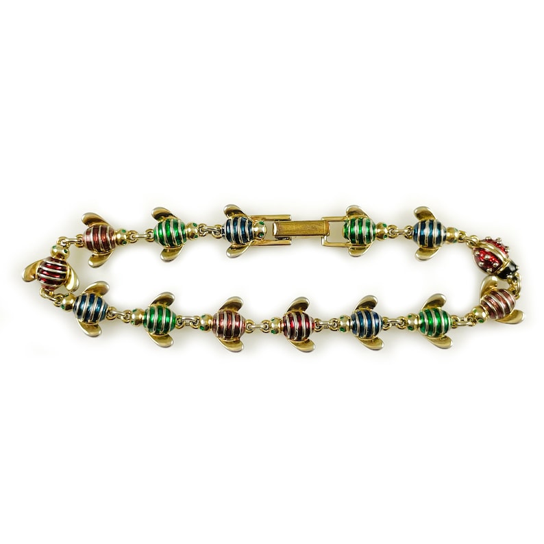May include: A gold bracelet with a series of bee-shaped charms. The bees are striped in red, green, and blue enamel.