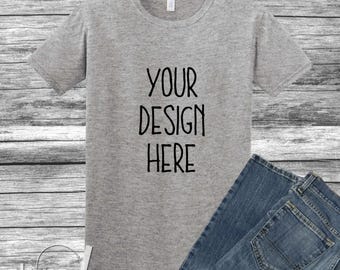 May include: A heather gray t-shirt with the text "YOUR DESIGN HERE" in black. The t-shirt is paired with blue denim jeans, creating a casual ensemble. The design is centered on the shirt.
