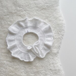 May include: White knitted ruffle collar with a bow tie detail. The collar is made of a soft, delicate yarn and has a delicate, feminine look.