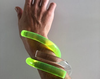 Op de afbeelding: Een set van drie armbanden, één transparant en twee neon groen, gedragen op een pols.