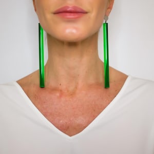 Peut inclure: Une femme portant un chemisier blanc à col en V avec de longues boucles d'oreilles rectangulaires vertes.