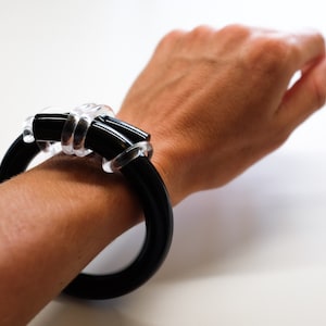 May include: A black and clear plastic bracelet with a unique knot design.