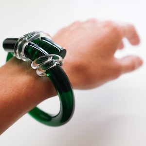 May include: A green glass bangle bracelet with a clear glass knot detail.