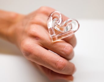 May include: A clear plastic ring shaped like a heart. The ring is worn on a finger.