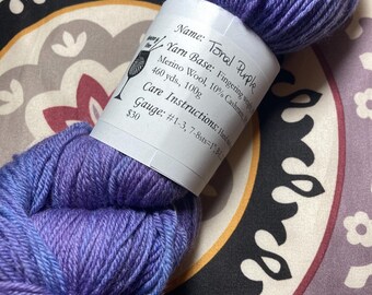 Può includere: Un gomitolo di lana viola etichettato "Tonal Purple" con le informazioni sulla base del filato: "Fingering weight, Merino Wool, 10% Cashmere, 460 yds., 100g". L'etichetta include anche le istruzioni per la cura e le informazioni sul calibro: "#1-3, 7-8sts=1", e ha un prezzo di 30 €.