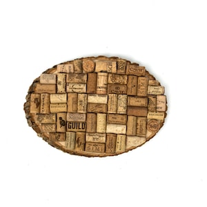 May include: A round wooden coaster with a cork mosaic design. The cork pieces are arranged in a pattern and have various labels and logos. The coaster has the word "GUILD" printed on it.
