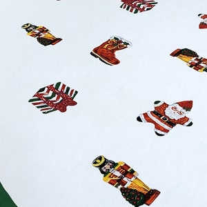 May include: A white circular tree skirt featuring a dark green border and a repeating pattern of Christmas-themed illustrations including Santa Claus figures, nutcrackers, wrapped gift boxes, and stockings in red, green, and gold colors.
