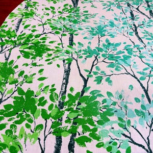 May include: A round, white tablecloth with a repeating pattern of stylized trees. The trees have black trunks and branches with green and teal leaves. The tablecloth is likely made of fabric.