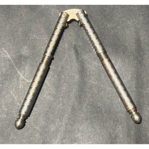 May include: A silver-colored nutcracker with textured handles and a hinge. The handles have a detailed pattern and end in rounded tips. The hinge area has the letters "HMO" stamped on it.