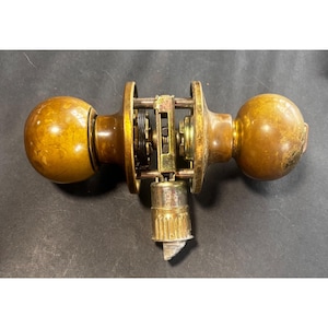 May include: Vintage brass doorknob set with a ball-shaped design. The set includes two knobs, a central mechanism, and a latch. The brass has a warm, aged patina, and the mechanism is visible, showcasing the internal components.