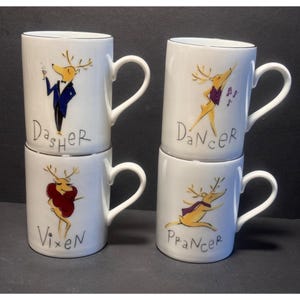 May include: Four white ceramic mugs with silver rims, each featuring a cartoon reindeer illustration and a name. The mugs are labeled Dasher, Dancer, Vixen, and Prancer, with each reindeer depicted in different clothing and poses on the front surface.