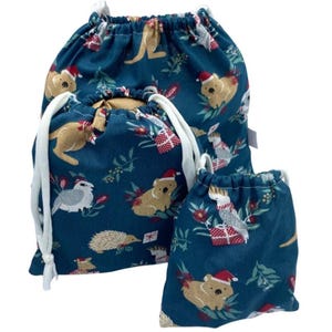 May include: Three teal drawstring bags of varying sizes featuring a repeating pattern of Australian animals including koalas, kangaroos, echidnas, and cockatoos wearing Santa hats, interspersed with red and white gift boxes and green foliage.