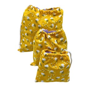 May include: Three yellow drawstring bags with a bee and honeycomb pattern. The bags are different sizes and are made of fabric.