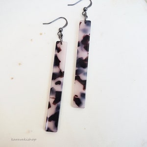May include: A pair of long, rectangular earrings with a black and white tortoiseshell pattern. The earrings have silver hooks.