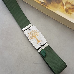 May include: A green bookmark with a silver charm featuring a gold tree design. The charm has a small green leaf attached to it.