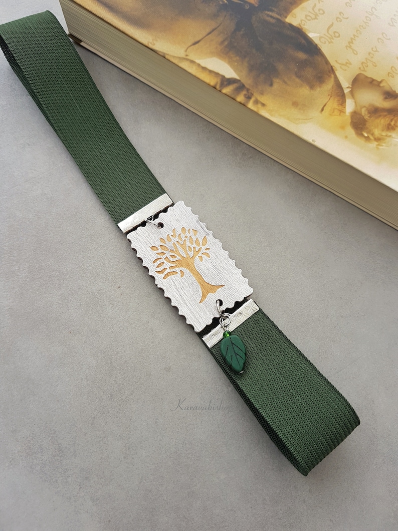 May include: A green bookmark with a silver charm featuring a gold tree design. The charm has a small green leaf attached to it.