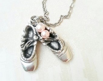 Può includere: Una collana d'argento con un ciondolo a forma di due scarpette da ballet e due perle rosa.