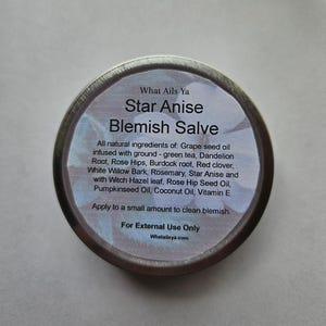 May include: A silver tin with a white label that reads "What Ails Ya Star Anise Blemish Salve". The label lists all natural ingredients including grape seed oil, green tea, dandelion root, rose hips, burdock root, red clover, white willow bark, rosemary, star anise, witch hazel leaf, rose hip seed oil, pumpkinseed oil, coconut oil, and vitamin E. The label also states "For External Use Only" and "Whatailsya.com".