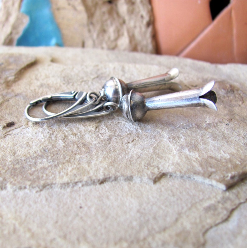 May include: Silver earrings with a flower-shaped design. The earrings are made of sterling silver and have a delicate, feminine look.