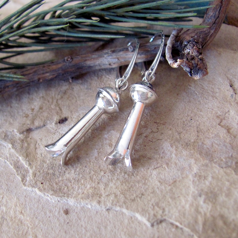 May include: A pair of silver earrings with a unique design. Each earring features a long, slender, cylindrical shape with a rounded top and a three-pronged bottom.