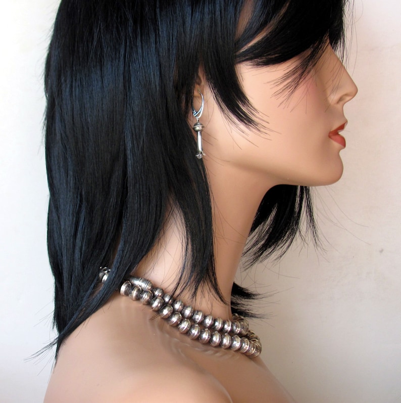 May include: A silver necklace with round beads. The necklace is worn by a woman with long black hair. The woman is wearing a silver earring in her left ear.