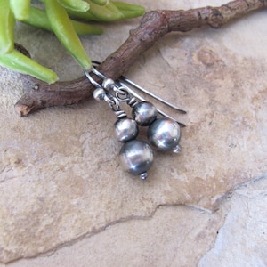 May include: A pair of dangle earrings featuring polished silver-toned spherical beads suspended from curved wire hooks. Each earring consists of two graduated round beads connected by a thin silver-toned wire, creating a simple and reflective metallic design.