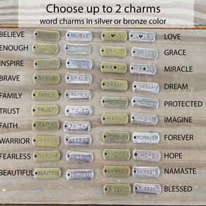 May include: A selection of word charms in silver and bronze colors. The charms include words like "Believe," "Inspire," "Family," and "Forever." The text "Choose up to 2 charms" is at the top.