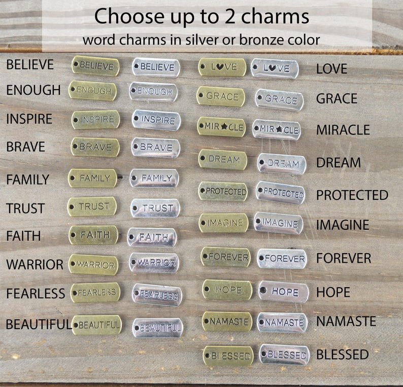 May include: A selection of word charms in silver and bronze colors. The charms include words like "Believe," "Inspire," "Family," and "Forever." The text "Choose up to 2 charms" is at the top.