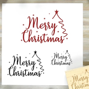 以下が含まれることがあります： 白い背景に、赤と黒の筆記体で「Merry Christmas」の文字と、様式化されたクリスマスツリーと星が描かれています。同じデザインの木製スタンプも表示されています。