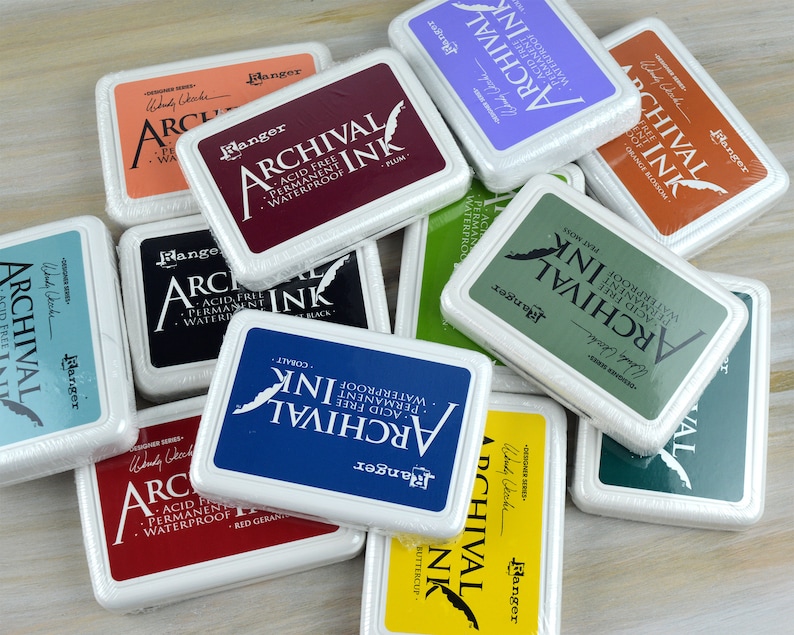 May include: A collection of Ranger Archival Ink pads in various colors, including red, blue, green, and orange. Each pad is labeled with the color name and the words "Archival Ink, Acid Free, Permanent, Waterproof". The pads are packaged in clear plastic.