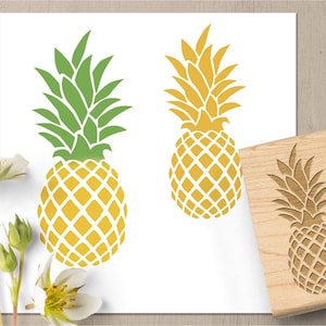 May include: Two pineapple designs in yellow and green, along with a wooden stamp featuring a pineapple carving. The designs are on a white background, with a wooden surface visible on the right side of the image. The pineapple designs are a tropical theme.