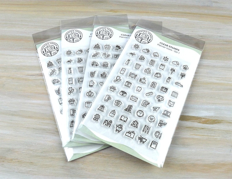 May include: Four clear stamp sets with various planner icons, including a book, clock, and shopping cart. Each set is packaged in a clear plastic sleeve. The text "CLEAR STAMPS Planner Icons - Set 1" is visible on the packaging.