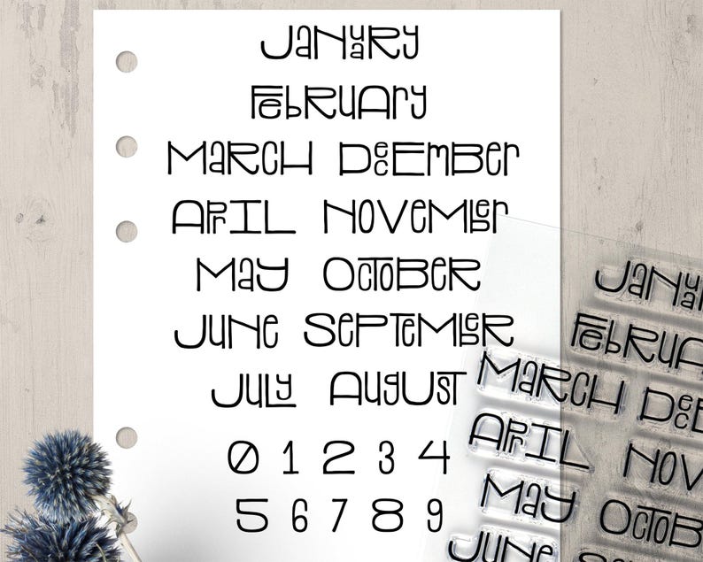 May include: A white paper with the months of the year and numbers printed in black. Clear stamps with the month names are visible on the right. The paper has three holes for binding.