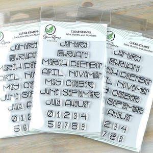 May include: Three clear stamp sets in plastic packaging. Each set contains months of the year and numbers. The text "CLEAR STAMPS Saba Months and Numbers" is printed at the top. The stamps are in a modern font.