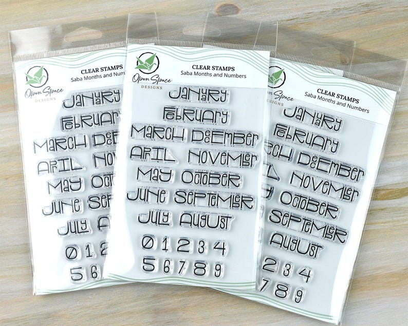 May include: Three clear stamp sets in plastic packaging. Each set contains months of the year and numbers. The text "CLEAR STAMPS Saba Months and Numbers" is printed at the top. The stamps are in a modern font.