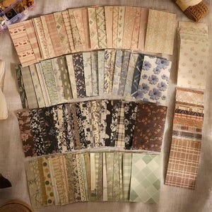 May include: A large collection of rectangular paper cards featuring a diverse array of patterns including floral prints, plaid, stripes, polka dots, and star motifs in various color palettes ranging from soft pastels to deep browns and greens.