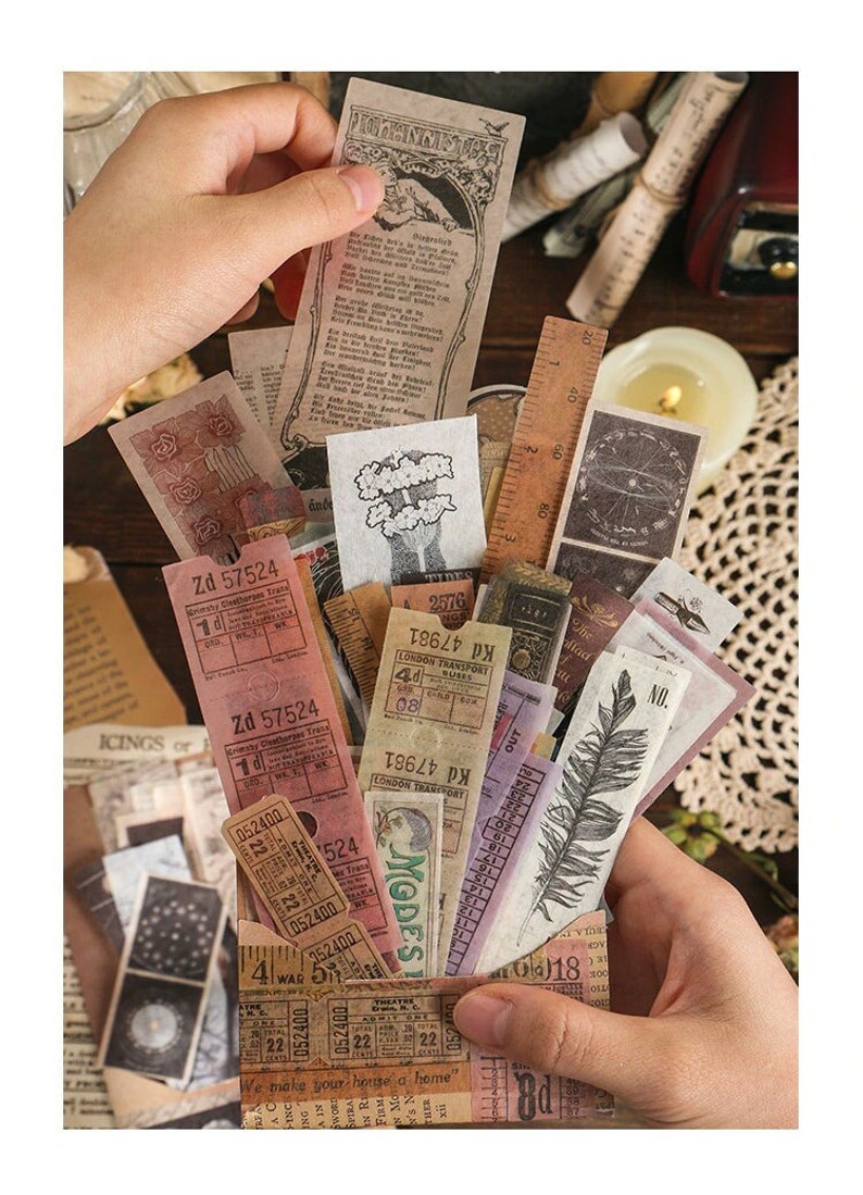 May include: A collection of vintage ephemera, including tickets, receipts, and decorative paper scraps, held in a person's hands. The items feature faded colors, aged textures, and various fonts. A wooden ruler and a lit candle are also visible.