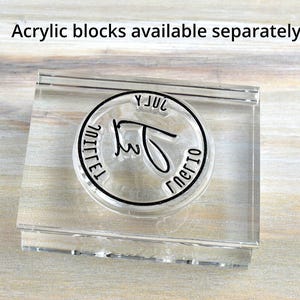 May include: Clear acrylic stamp with a circular design. The stamp has a black border with the words "JUL" and "nerio" in a handwritten font. The text "Acrylic blocks available separately" is above the stamp.