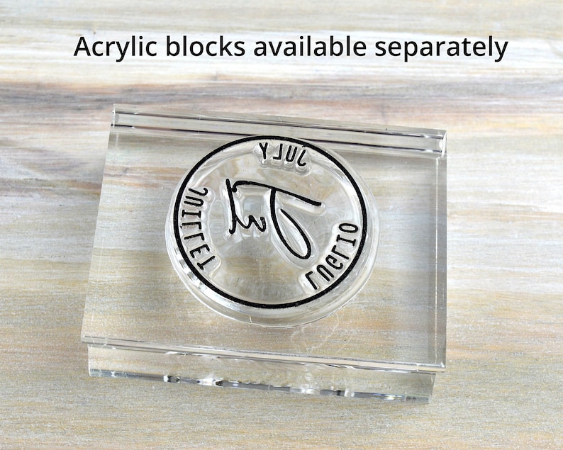 May include: Clear acrylic stamp with a circular design. The stamp has a black border with the words "JUL" and "nerio" in a handwritten font. The text "Acrylic blocks available separately" is above the stamp.