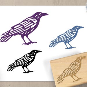 May include: A collection of raven illustrations in purple, blue, and black, alongside a wooden stamp with a raven design. The raven images are detailed with wing and body patterns, suitable for art or craft projects.