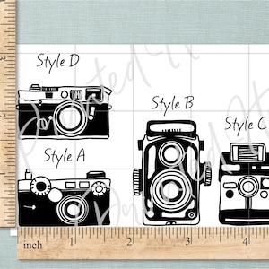 May include: Black and white illustrations of four vintage cameras, labelled Style A, B, C, and D. The cameras have different designs, including lenses, viewfinders, and flash attachments. The background features a grid pattern.